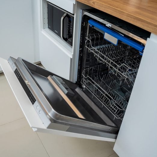 The white kitchen and opened dishwasher with clean dishes